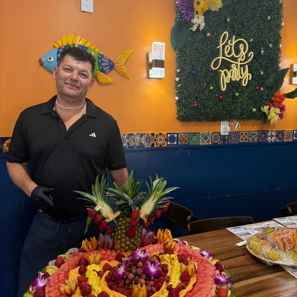 A man standing beside a decorative fruit platter in the restaurant dining room.